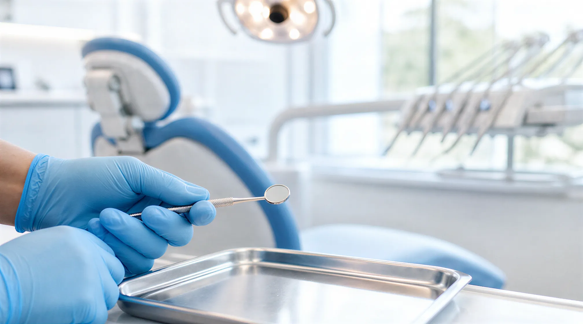 Blaue Einweghandschuhe halten ein poliertes Dentalinstrument über einem sterilen Behandlungstablett.