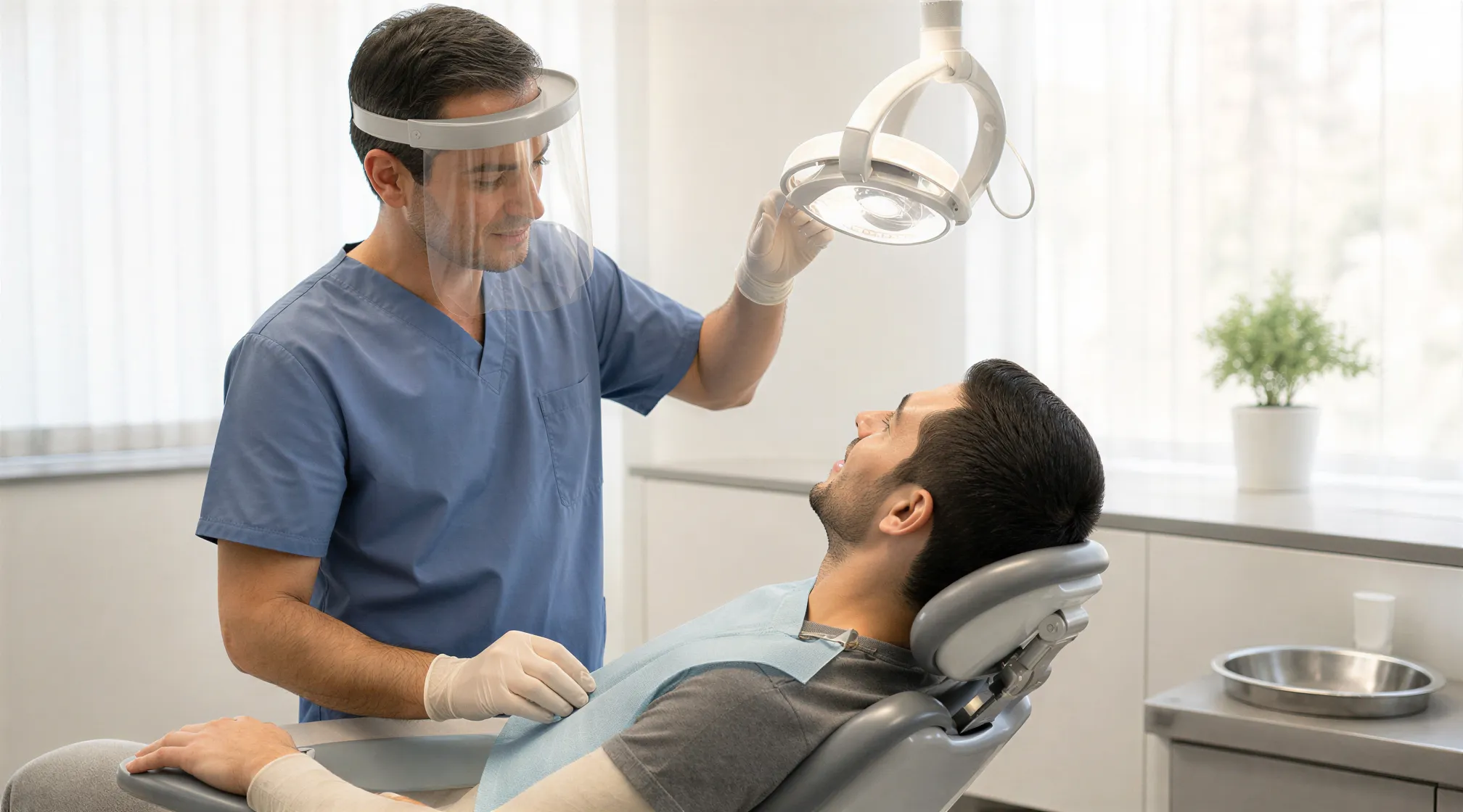 Eine Zahnärztin in blauer Kleidung justiert eine moderne Beleuchtung über der Hand eines Patienten in einem hellen